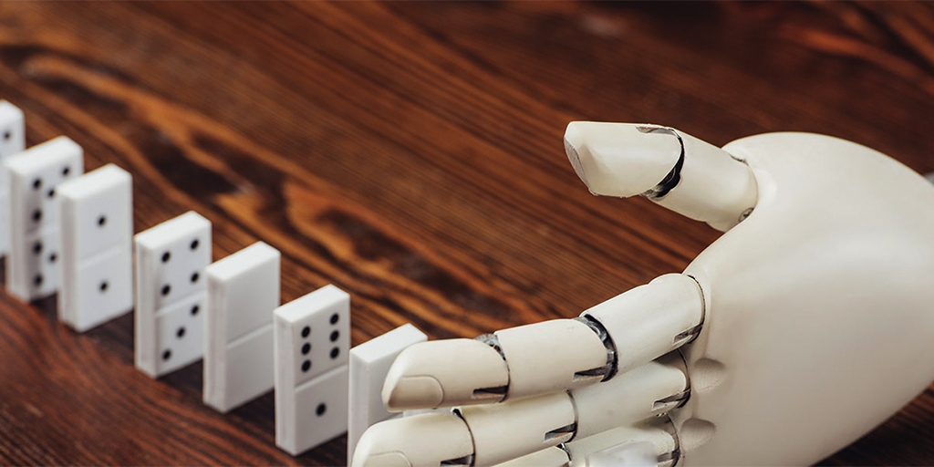 Image of a robot hand about to knock over a line of dominoes.